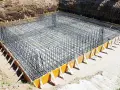 Siatka zbrojeniowa w wykopie pod fundamenty, gotowa do zalania betonem. Pokazuje, jak łączyć zbrojenie w fundamentach.