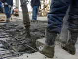 Beton na fundamenty wylewany jest na zbrojenie. Pracownicy w gumowcach nadzorują proces.