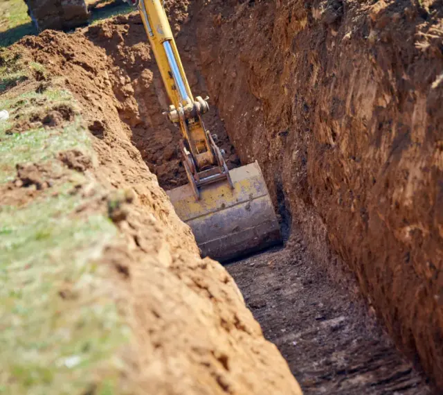 Koparka pogłębia wykop pod garaż. Widać jaki głęboki fundament pod garaż powstaje.
