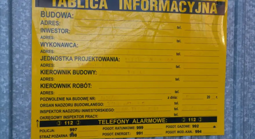 Tablica informacyjna budowy, gdzie można znaleźć dane o pozwoleniach na budowę domu, wykonawcach i numerach alarmowych.