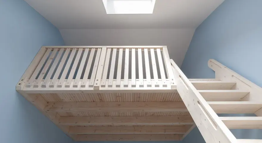 Jasna, drewniana antresola z balustradą i schodami, podświetlona przez okno dachowe.