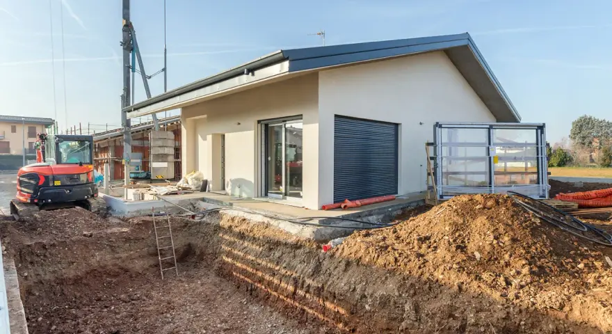 Budowa domu 70m2. Wykop pod fundamenty, koparka i częściowo wykończony budynek.