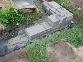 Fundamenty z betonu i bloczków, częściowo zalane, otoczone trawą. Pytanie, czy można zostawić odkryte fundamenty na zimę, jest tu kluczowe.