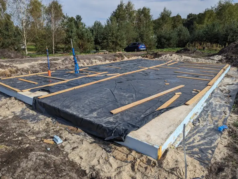 Płyta fundamentowa z folią i drewnianymi elementami na budowie domu szkieletowego.